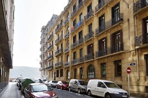 A street lined with multi-story buildings, parked cars, and a no entry sign.
