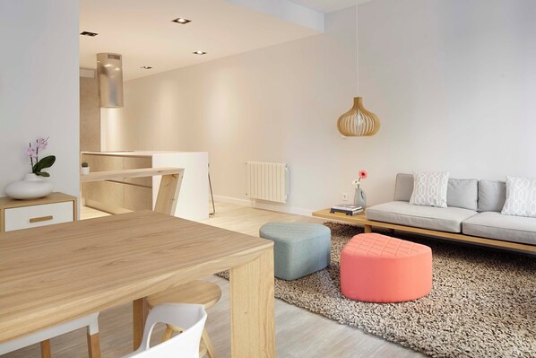 A modern living room with a wooden dining table, a sofa, and a pink ottoman. - Soraluxe by FeelFree Rentals (San Sebastián)