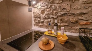 A kitchen with a stone wall, a black induction cooktop, a wooden cutting board with a pumpkin, and a yellow tray with a bottle and a bowl. - Petrella's Point Studio (Vernazza)