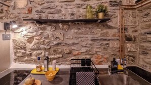 A kitchen with a stone wall, a shelf with glasses, a bottle, a bowl, and a sink. - Petrella's Point Studio (Vernazza)