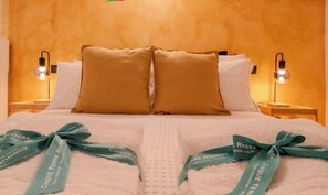 A hotel room with a bed, two pillows, two nightstands with lamps, and a towel with a ribbon. - Petrella's Point Studio (Vernazza)