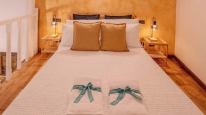 A neatly made bed with two pillows, two bedside tables with lamps, and a wooden floor. - Petrella's Point Studio (Vernazza)