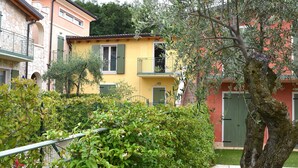 Ein gelbes Gebäude mit Balkon, umgeben von Grünflächen und anderen Häusern.