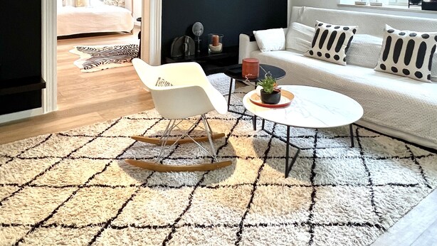 Een moderne woonkamer met een zwarte muur, een witte bank, een witte fauteuil, een ronde salontafel en een hanglamp.