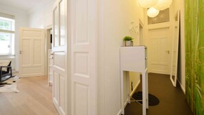 Een hal met witte deuren, een kleine witte tafel met een plant, en een groene muur met een bamboepatroon.