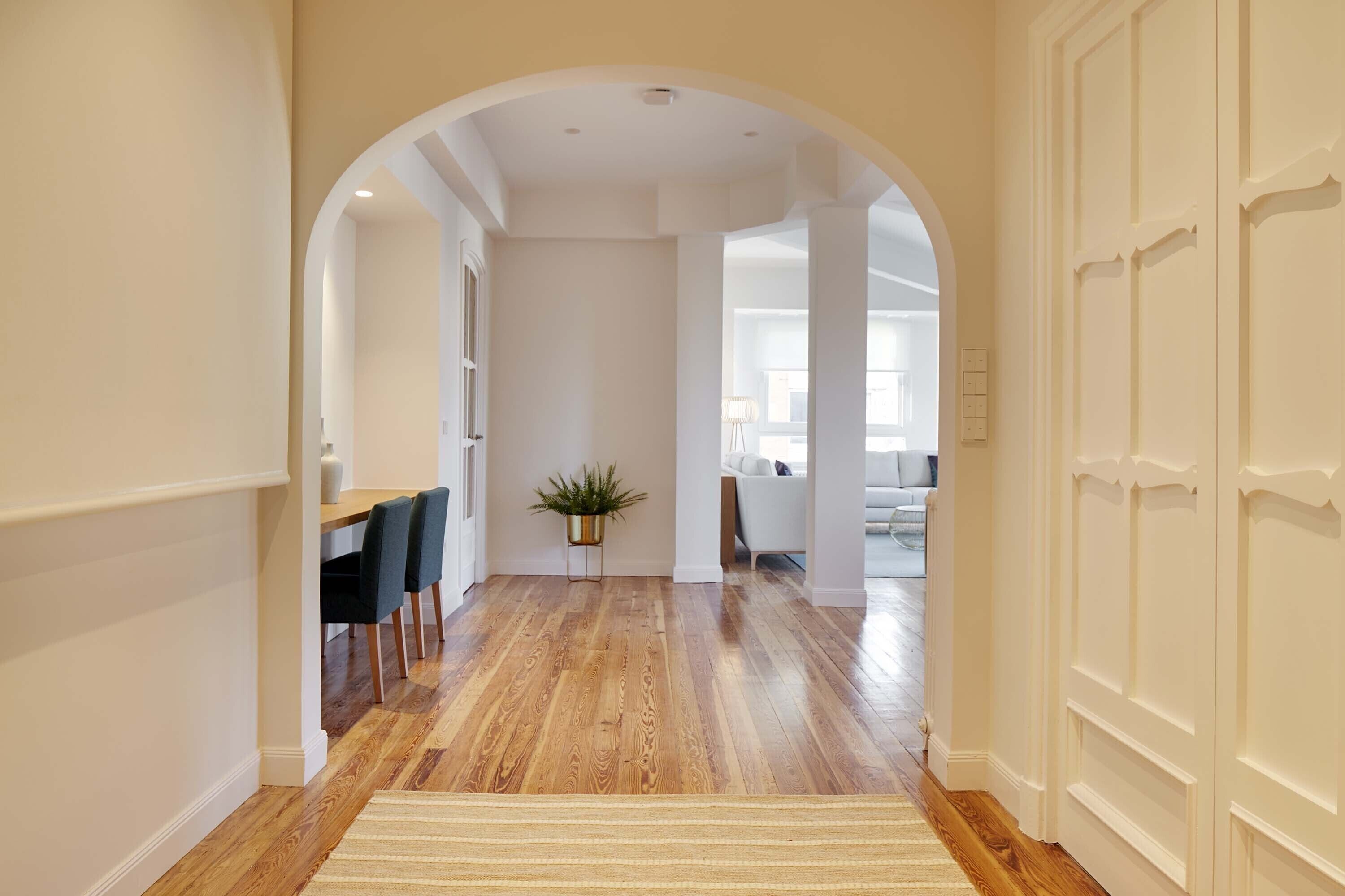 A hallway with wooden flooring, a dining area with chairs and a table, and a potted plant.