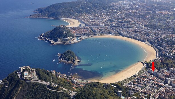 An aerial view of a coastal city with a large bay, a beach, and a densely built urban area.