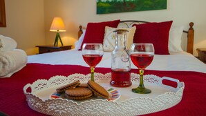 Un letto rifatto con cura, con una coperta rossa, un vassoio con biscotti e bicchieri di bevanda rossa e un quadro raffigurante un albero appeso al muro.