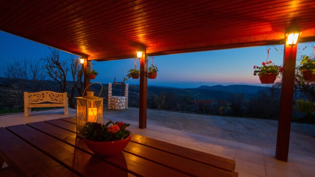 Patio esterno con panche in legno, fioriere appese e un muro in pietra.
