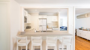 A modern kitchen with a central island, white cabinetry, and a seating area with white chairs. - Hayes @ Jervis Bay - Pet Friendly Award Winner - 4 Mins to Beach (Callala Beach)