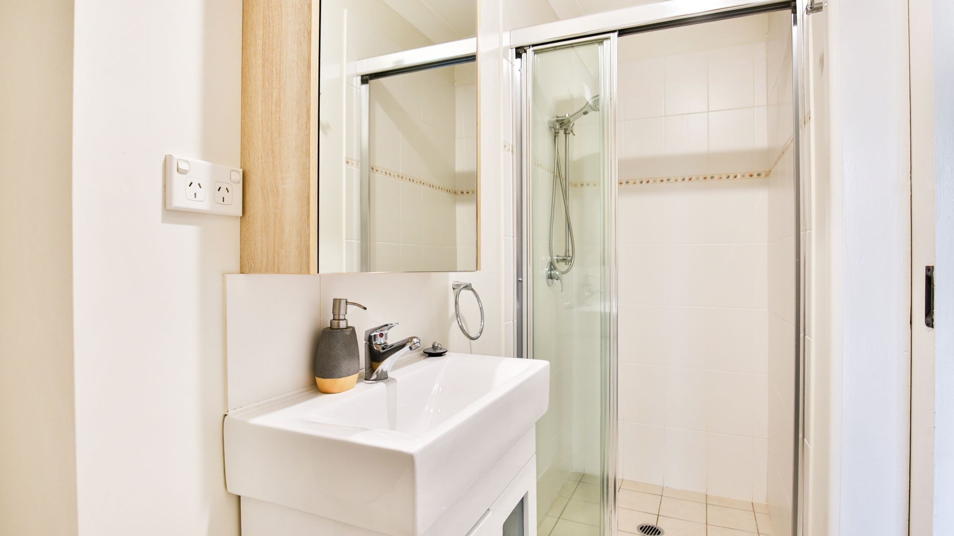 A modern bathroom with a white sink, a mirror, and a glass-enclosed shower.