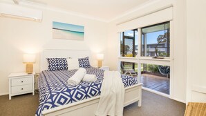 A bedroom with a large bed, two bedside tables, a window with a view of the outside, and a painting on the wall. - Hayes @ Jervis Bay - Pet Friendly Award Winner - 4 Mins to Beach (Callala Beach)