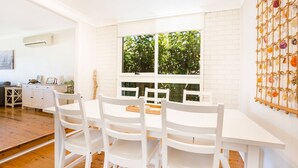 Una habitación luminosa y blanca con un ventanal grande, muebles blancos y un adorno en la pared.