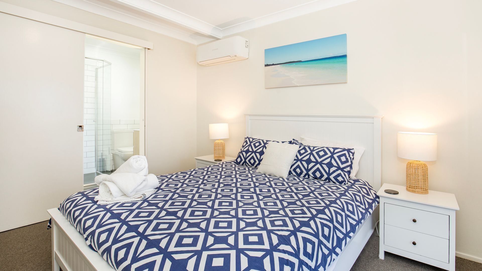 Une chambre à coucher avec un lit, des tables de chevet, un tableau et un appareil de climatisation.