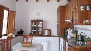 A kitchen with wooden beams, a dining table with chairs, and a clock on the wall.