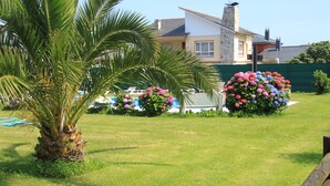 A well-maintained lawn with a palm tree and flowering bushes, a pool, and a house with a stone facade.