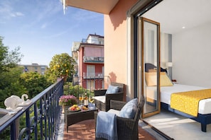 Un balcon agrémenté de meubles en osier, une table à manger avec des fruits et du vin, et un lit recouvert d’une couvre-lit à motifs jaunes.