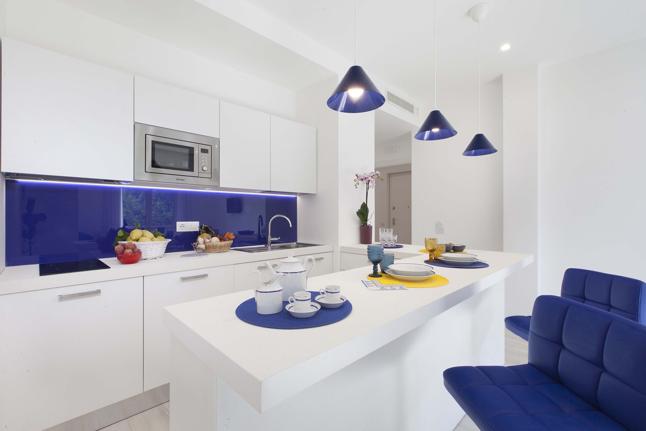 A modern kitchen with white cabinets, a built-in microwave, and a central island with blue accents.