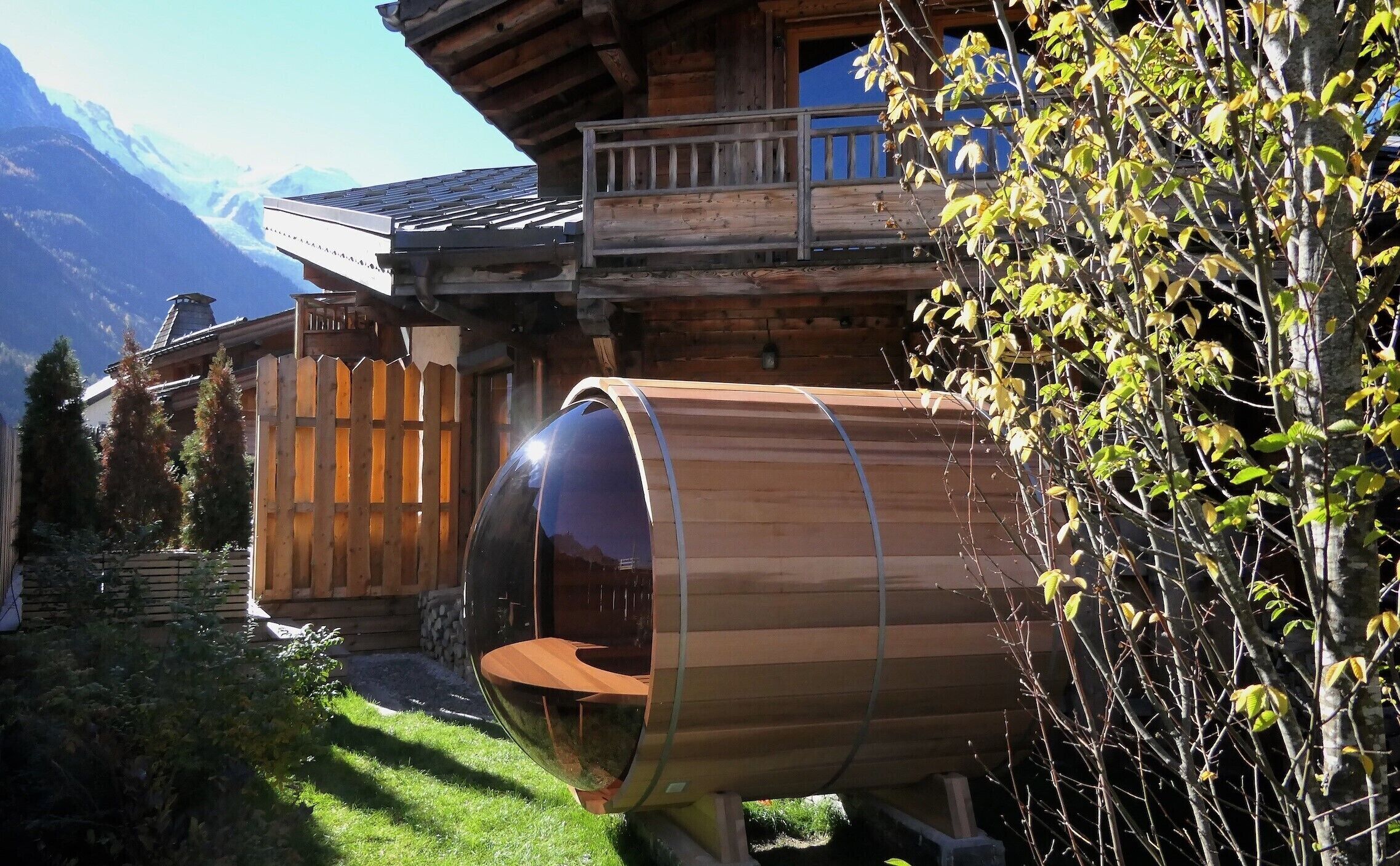 A wooden cabin with a glass-enclosed room, a wooden deck, and a mountain backdrop.