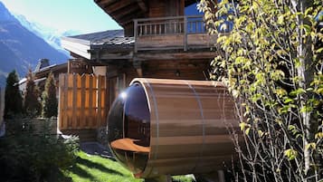 A wooden cabin with a glass-enclosed room, a wooden deck, and a mountain backdrop.