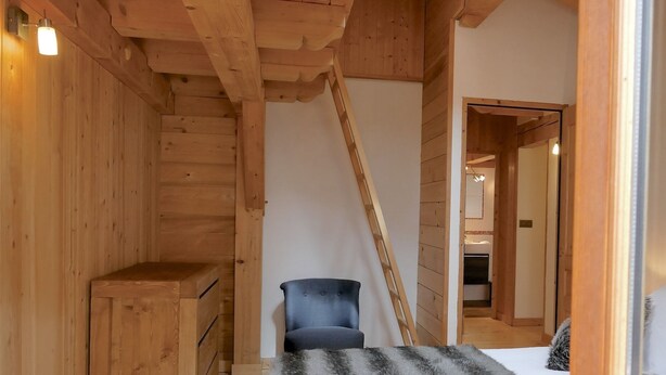 L’intérieur d’une cabane en bois, avec un lit en mezzanine, une chaise et un escalier.