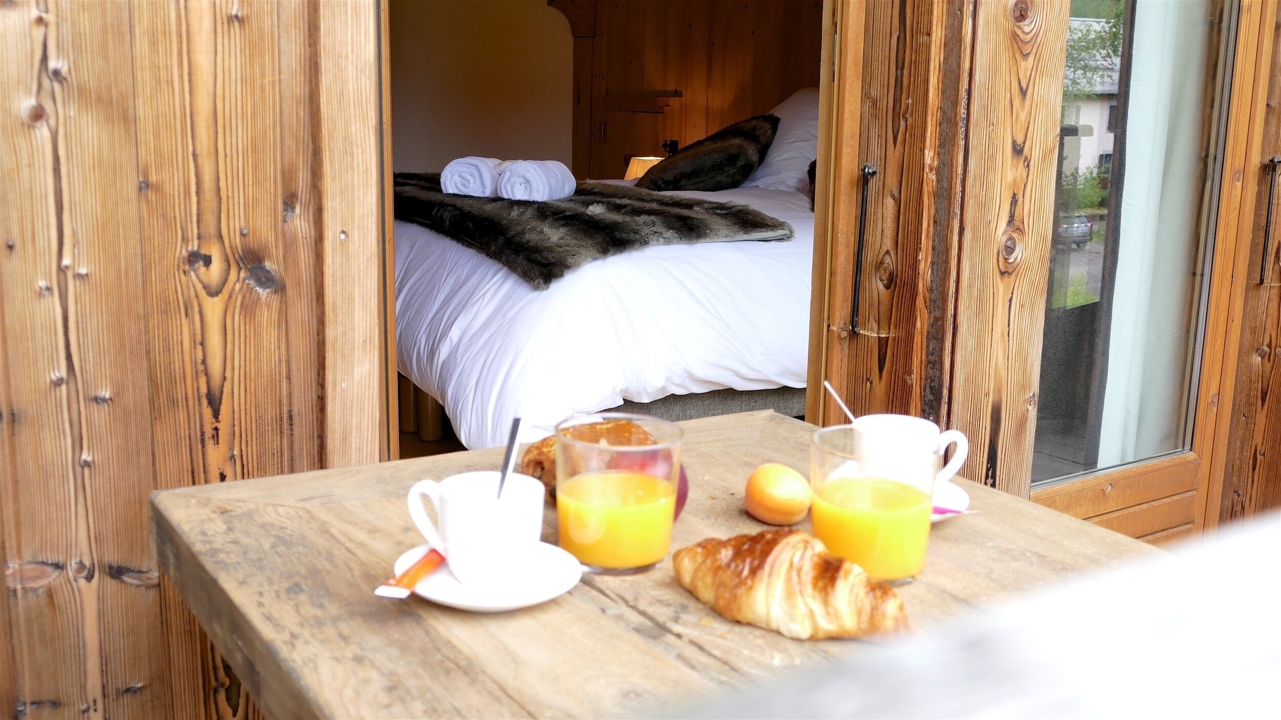 Una mesa de madera con alimentos para el desayuno, como cruasanes, jugo y una taza.