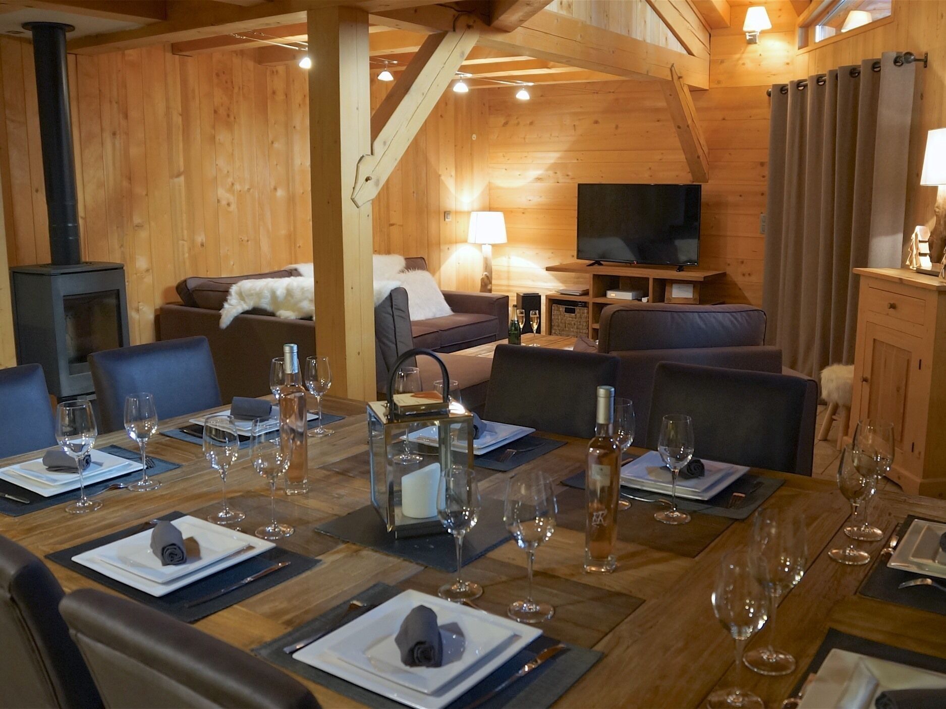 Un intérieur chaleureux en bois, avec un coin repas aménagé pour prendre un repas, un salon avec un canapé et un téléviseur, et une cheminée.