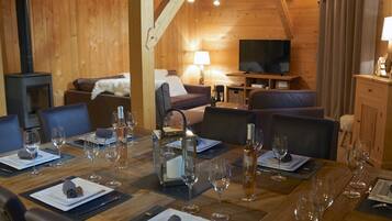 A cozy wooden interior with a dining area set for a meal, a living room with a sofa and a TV, and a fireplace.