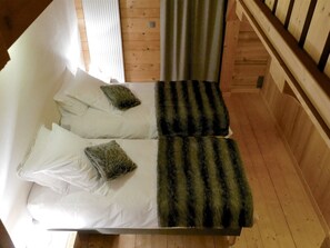 Una cama con sábanas blancas y dos almohadas de estampado verde y negro a rayas.