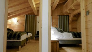 Una cabaña de madera con dos camas, cada una con una cortina verde y una mesita.