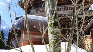 Une cabane en bois, dont le toit est recouvert de neige, entourée d’arbres et de montagnes.