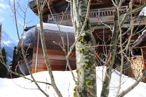 Une cabane en bois, dont le toit est recouvert de neige, entourée d’arbres et de montagnes.