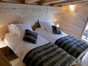 Une chambre dans un chalet en bois, avec deux lits, du linge de lit blanc et un plaid en fourrure sur chaque lit.