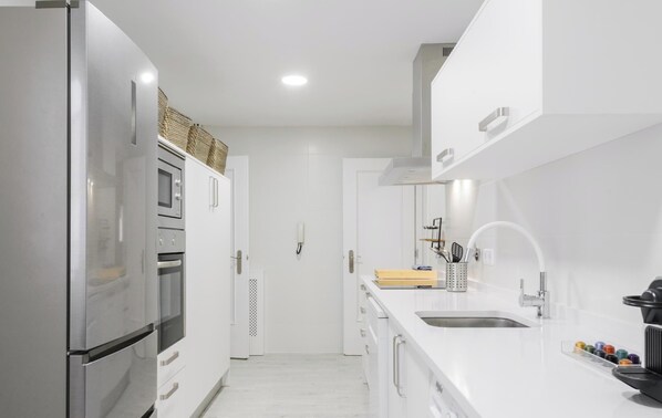 Eine moderne Küche mit weißen Schränken, Edelstahlgeräten, einem Backofen und einem Spülbecken mit Armatur.