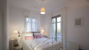A bedroom with a four-poster bed, bedside tables with lamps, a window with sheer curtains, and a radiator. - Kallisti Rodia  · Dream Villa with Views Garden nr (Santa Maria)