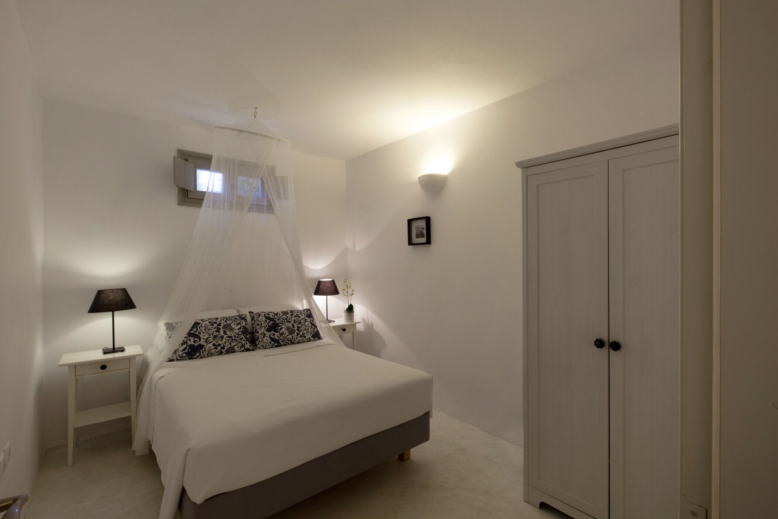 A bedroom with a bed, bedside lamps, a nightstand, a wardrobe, and a wall-mounted air conditioning unit.