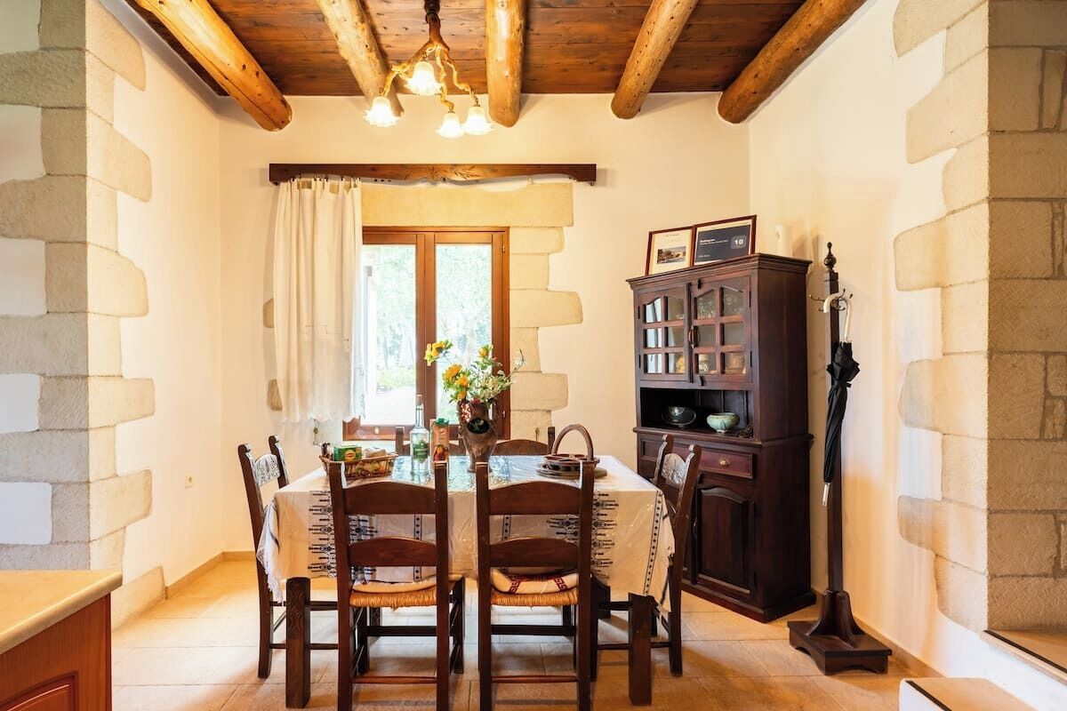 Un comedor con techo de madera, paredes de piedra, una mesa de comedor con sillas, un aparador y una ventana con cortinas.