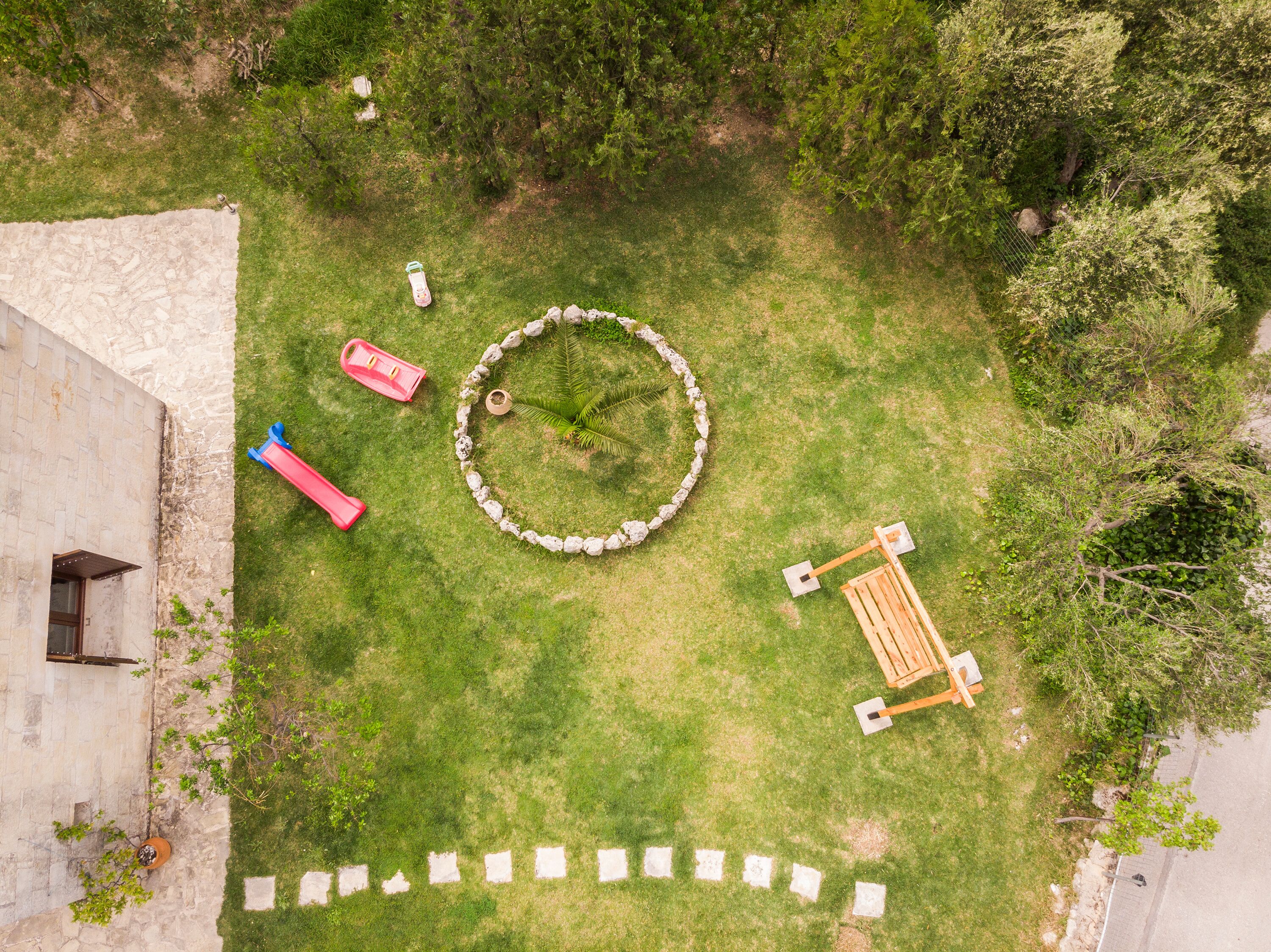 Vue aérienne d’une cour intérieure avec un mur en pierre, un motif circulaire en pierre et un banc en bois.