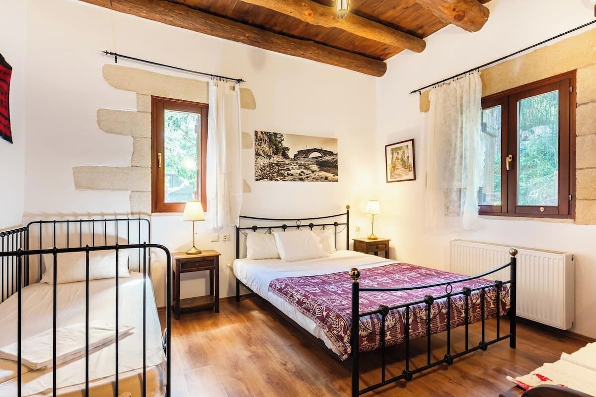 A bedroom with a bed, a nightstand, a chair, a window with curtains, and a painting on the wall.