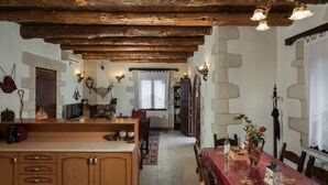 A rustic interior with exposed wooden beams, a stone wall, a dining table with a red tablecloth, and a chandelier.