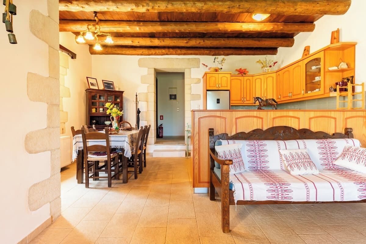 Ein gemütliches Wohnzimmer mit einer Couch, einem Holzespeisetisch und Stühlen. Es gibt eine Küchenzeile mit Holdekor und einem Kühlschrank.