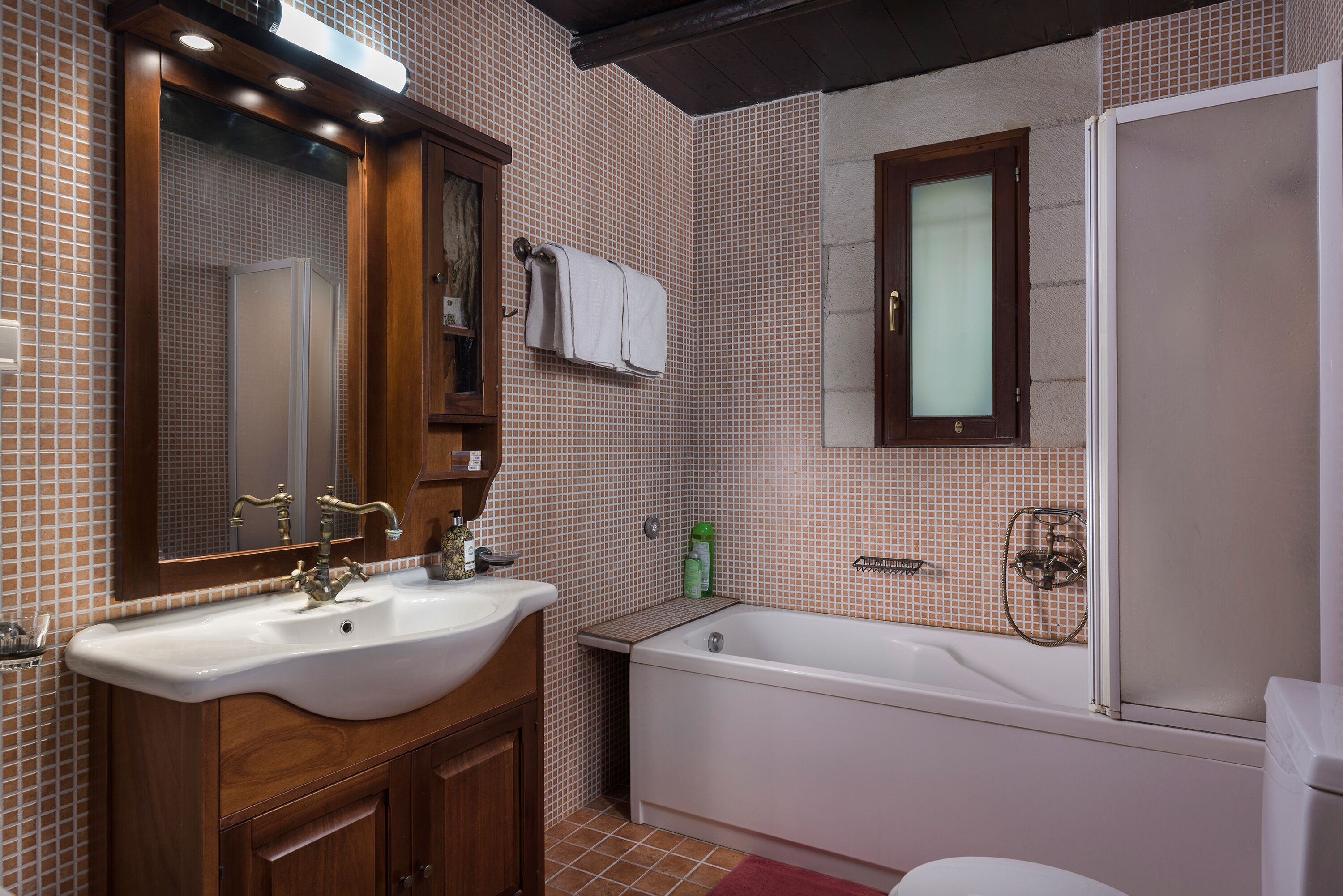A bathroom with a wooden vanity, a white sink, a bathtub, and a toilet.