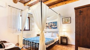A bedroom with a four-poster bed, wooden flooring, a window with curtains, a bedside table with a lamp, and a framed picture on the wall.