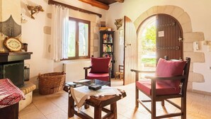 A cozy room with a fireplace, two red chairs, a wooden table, a bookshelf, and a stone archway.