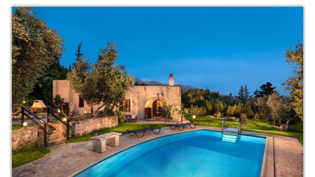 A stone building with an arched entrance, a swimming pool, and outdoor seating.
