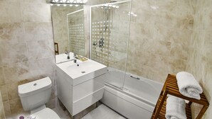 Un baño moderno con inodoro, lavabo, espejo, ducha y un perchero de madera.