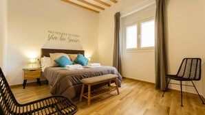 A bedroom with a bed, a bench, a chair, a nightstand, and a wall with a motivational quote. - Balcones de CANDELARIA by Cadiz4Rentals (Cádiz)