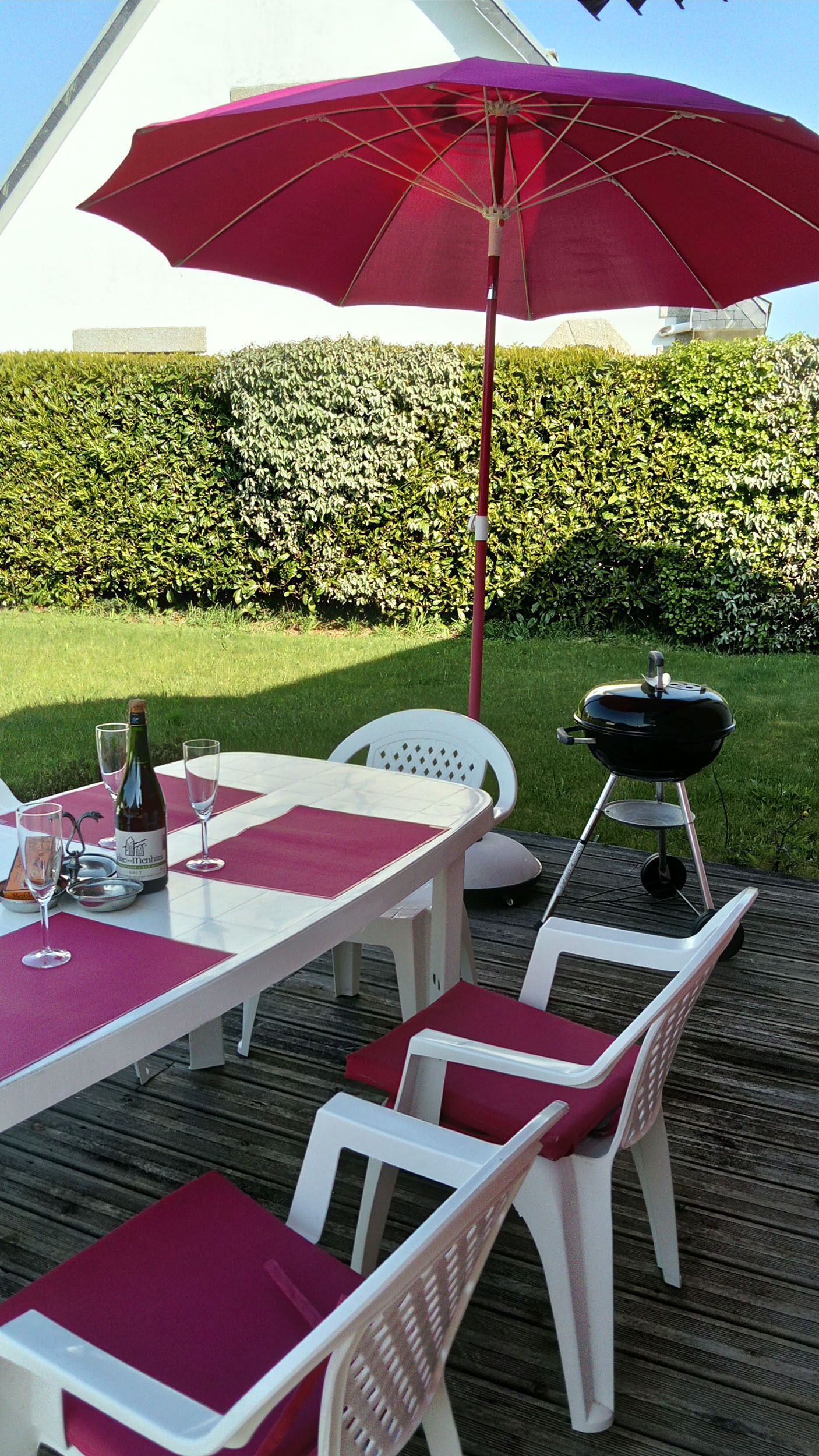 En utomhusplats med ett bord för två, en grill och ett stort parasoll som ger skugga.