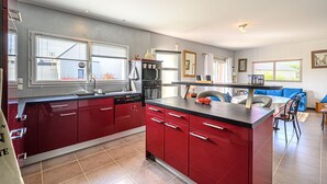 A modern kitchen with red cabinets, a central island, and a dining area with blue chairs. - GROUND FLOOR, 3 BEDROOMS, 5 MINUTES FROM THE BEACH, DOG ALLOWED (Treffiagat)