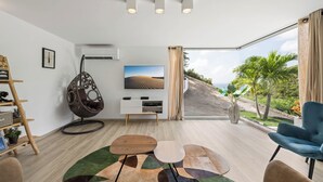 A modern living room with a large window, a hanging chair, a flat-screen TV, and a wooden coffee table. - SUNSET VILLA ANGEL **** (saint barthelemy)